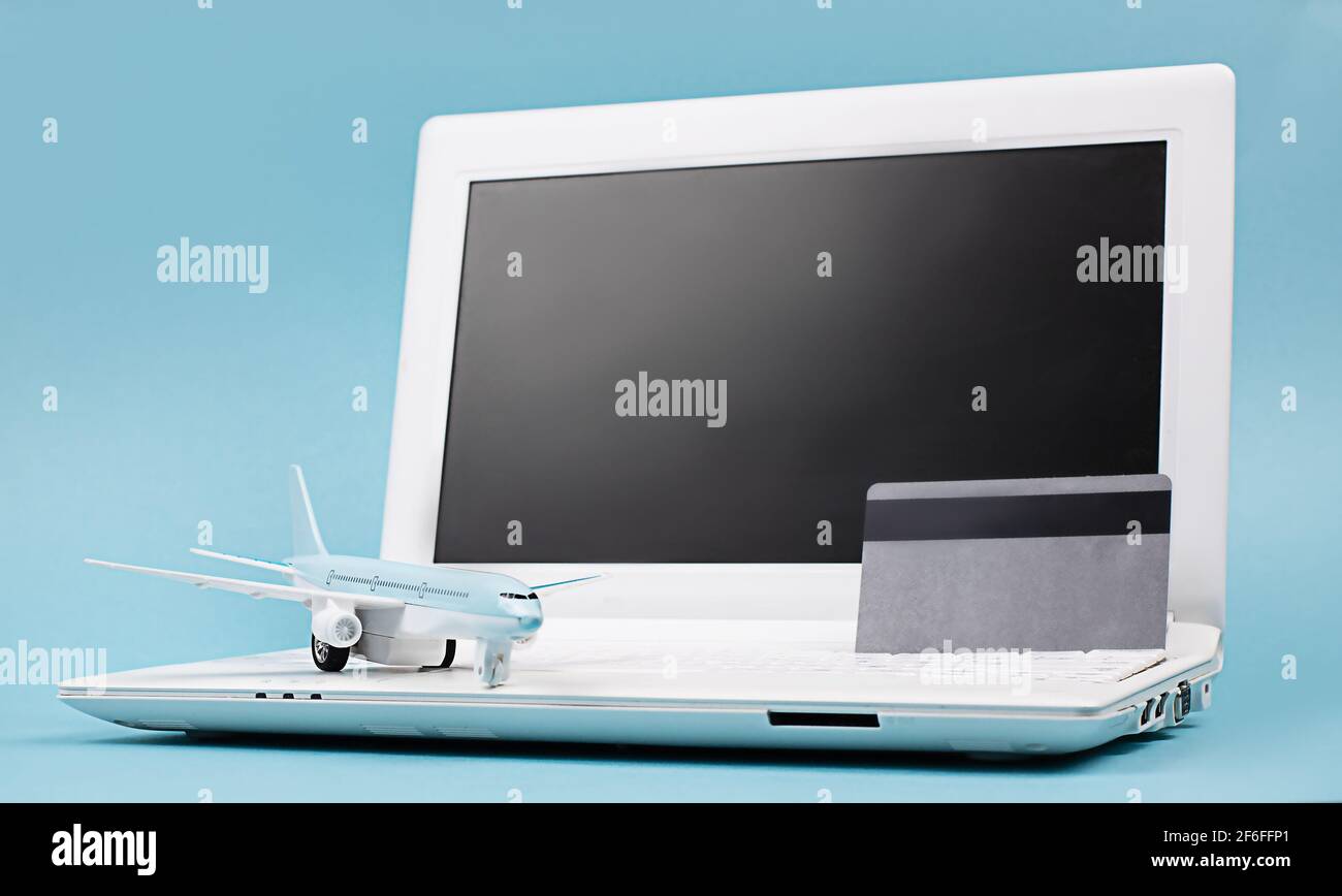White laptop on a blue background, black screen.  Nearby is a bank card and a miniature airplane.  Concept - Online booking of air tickets, travel Stock Photo