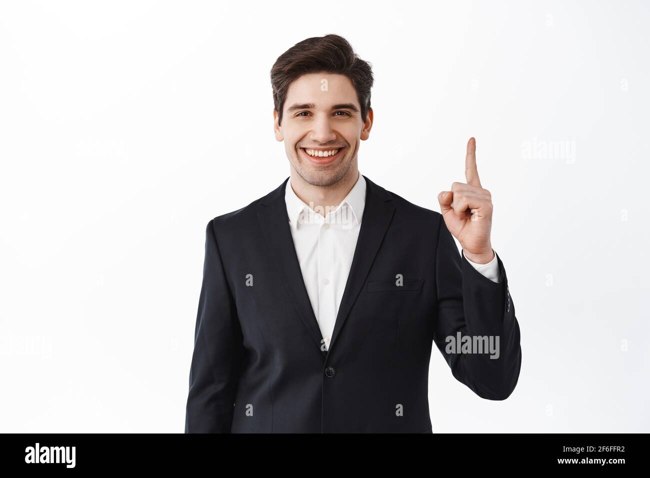 Confident male real estate agent, broker business man in suit pointing finger up, showing top advertisement, deal on market, standing over white Stock Photo