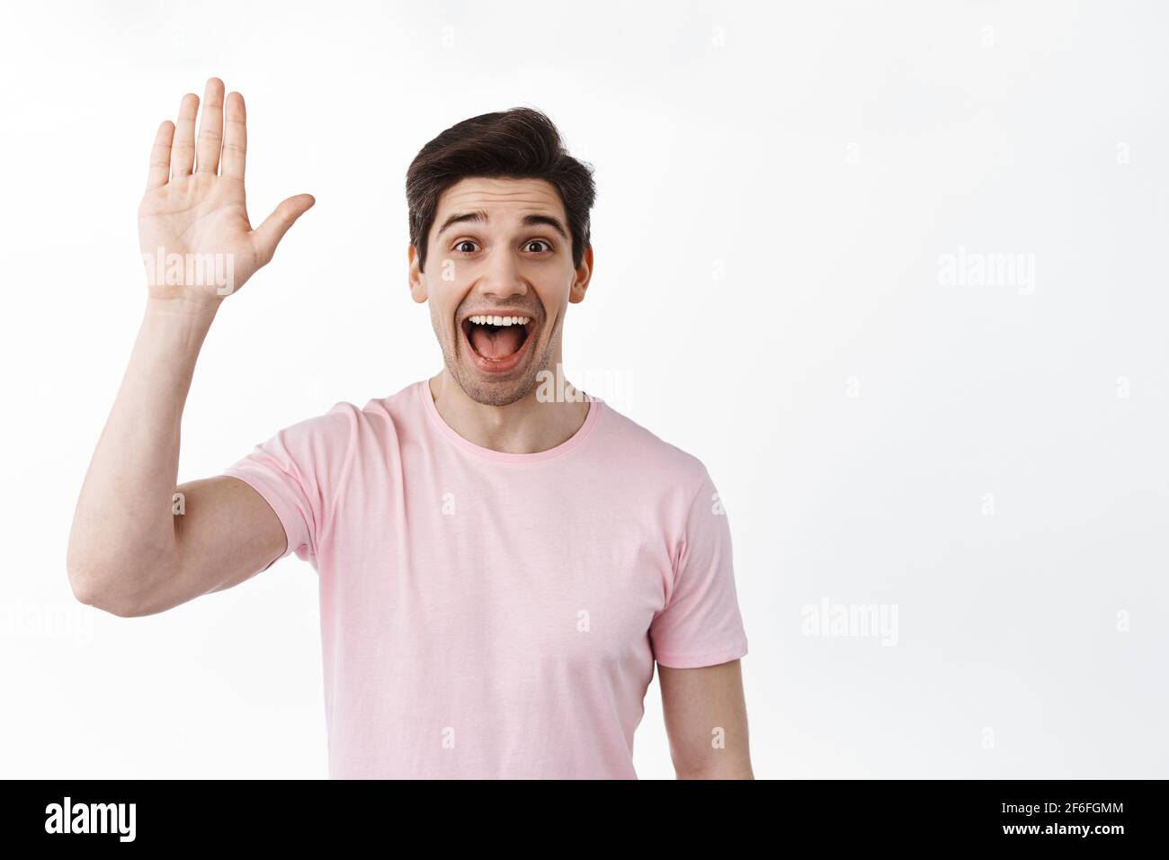 Excited friendly man waving hand and say hey, hello greeting gesture, extremely happy to see you, standing against white background in casual clothes Stock Photo