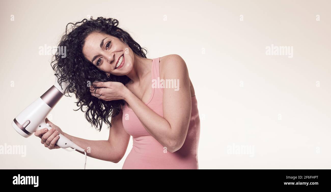 young black curly haired woman follows the curly girl method with suitable curly hair care products using a blow dryer to get curls and waves in her h Stock Photo