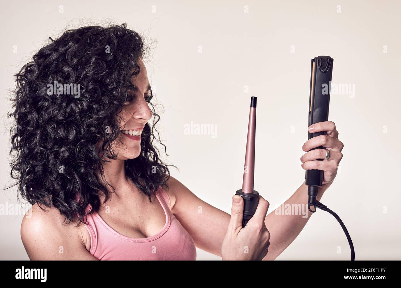 Young smiling curly-haired woman in profile holds a hair curler and a hair straightener. care and beauty concept Stock Photo