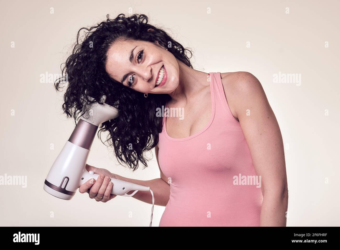 Young smiling curly haired woman follows the curly girl method with suitable curly hair care products using a blow dryer to get curls in her hair. car Stock Photo