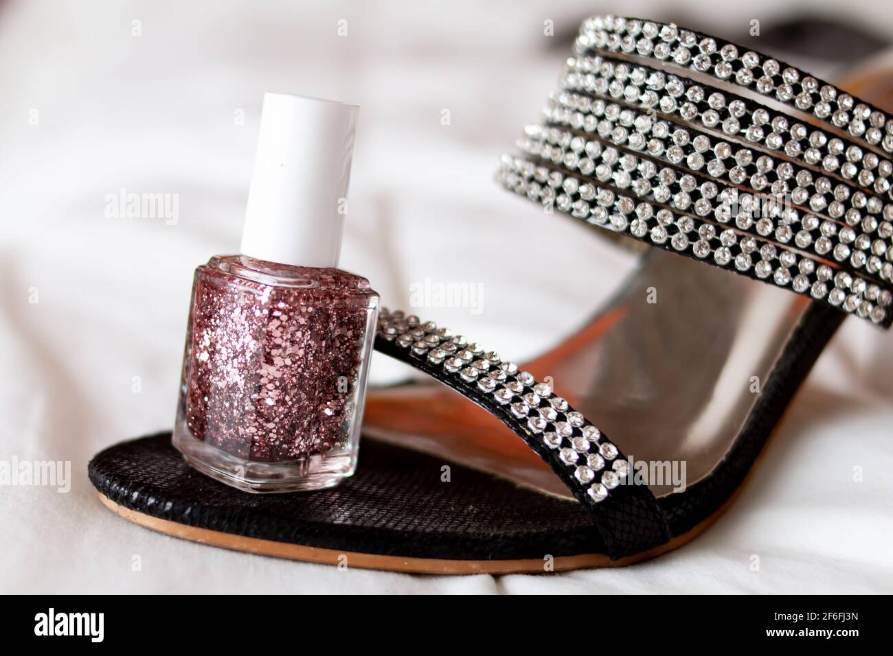 Soft-focus, glittery nail polish to match a glittery bedazzled two inch high heel shoe on a white bed sheet, isolated, Ontario Canada 2021. Stock Photo