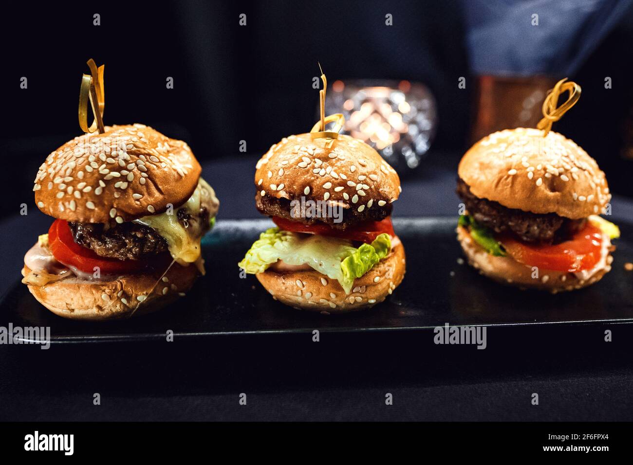 Three mini burgers on a black rectangular elongated stand. Stock Photo