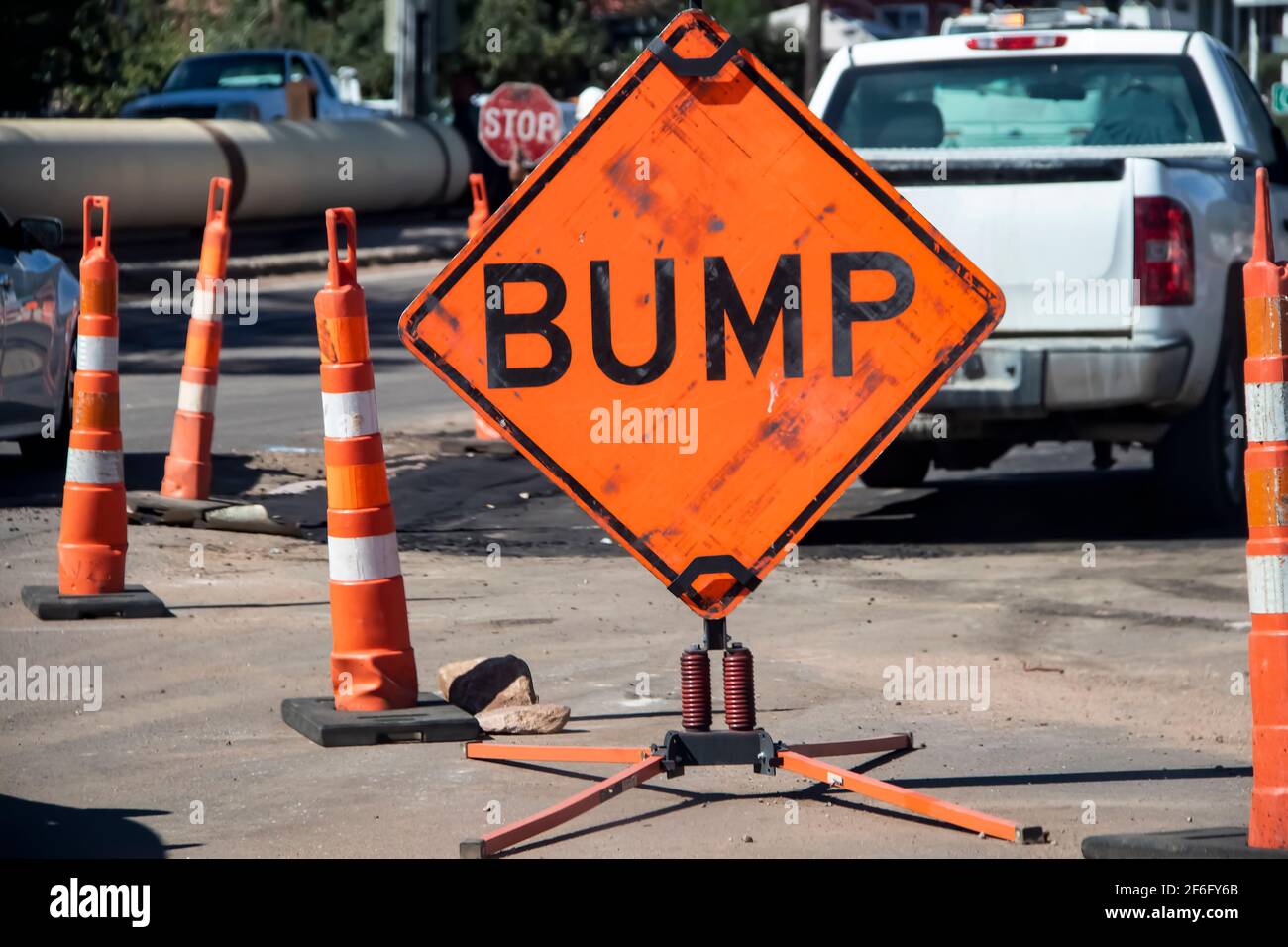Big orange grungy sign that says BUMP surrounded by highway construction cones with trucks and torn up pavement in the background - selective focus Stock Photo