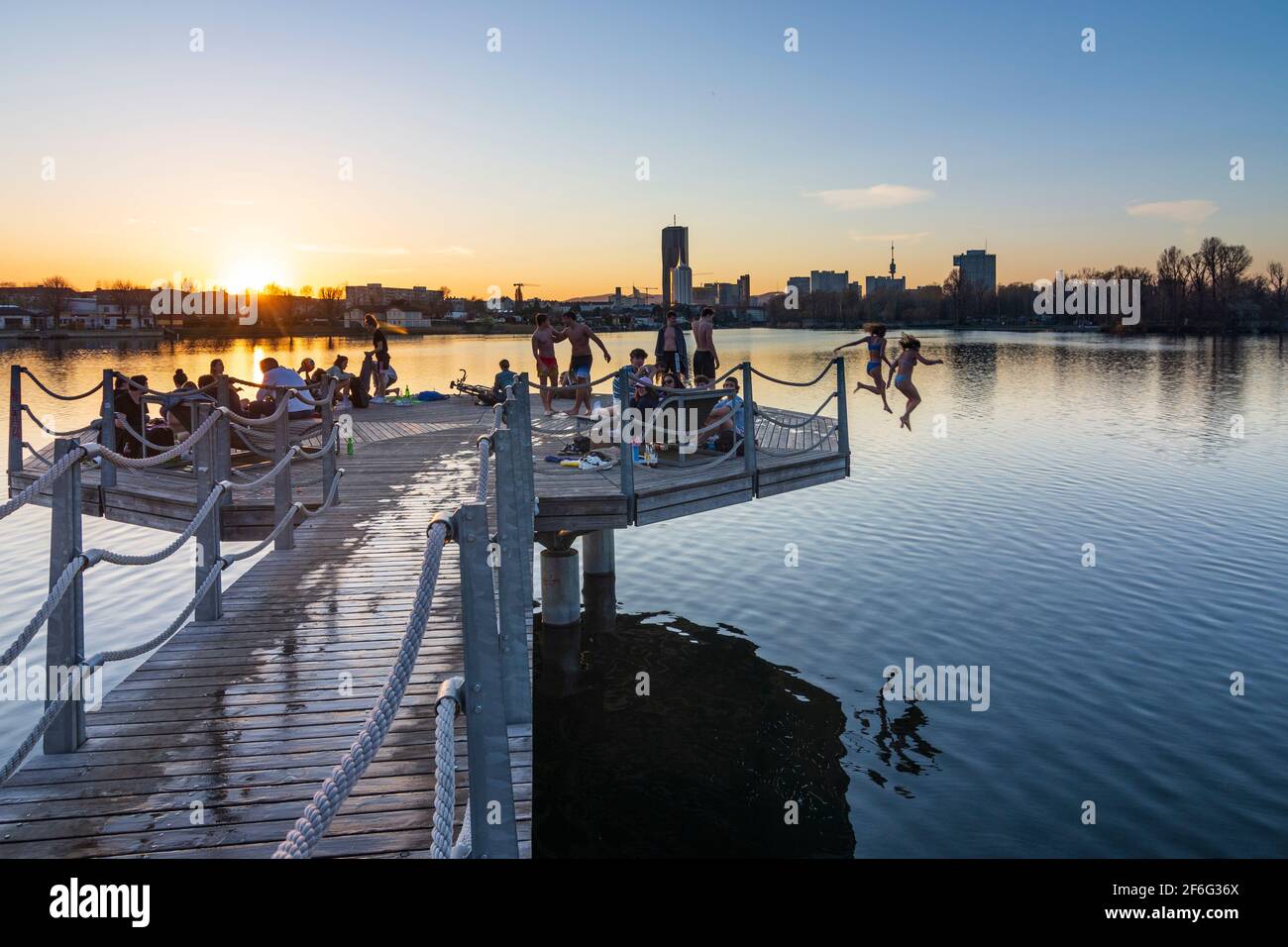 Wien, Vienna: girls jump into water of oxbow lake Alte Donau (Old Danube),  young people sitting on a platform above the lake, sunset, buildings of Don  Stock Photo - Alamy