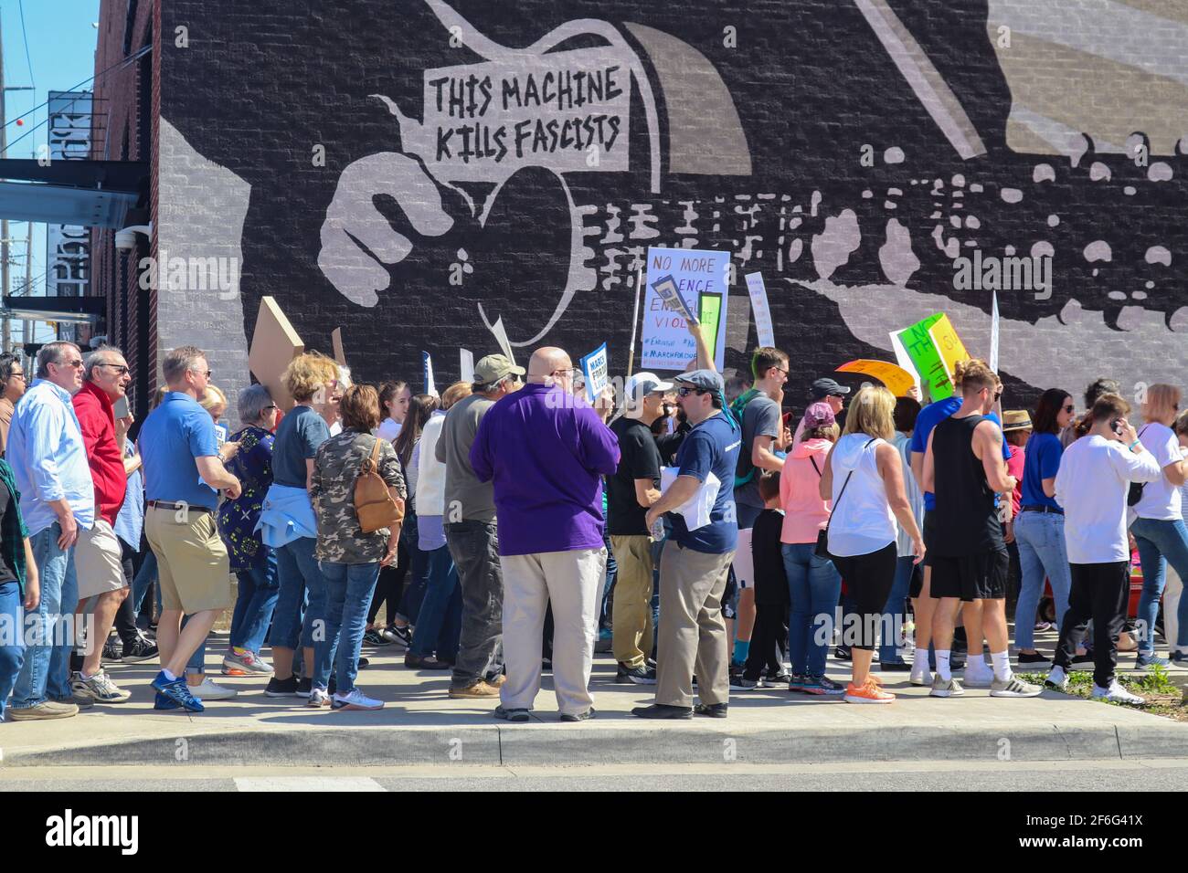 Protestors walk past Wood Guthrie mural that says This Machine Kills Fascists n Tulsa Oklahoma USA 3 24 2018 Stock Photo