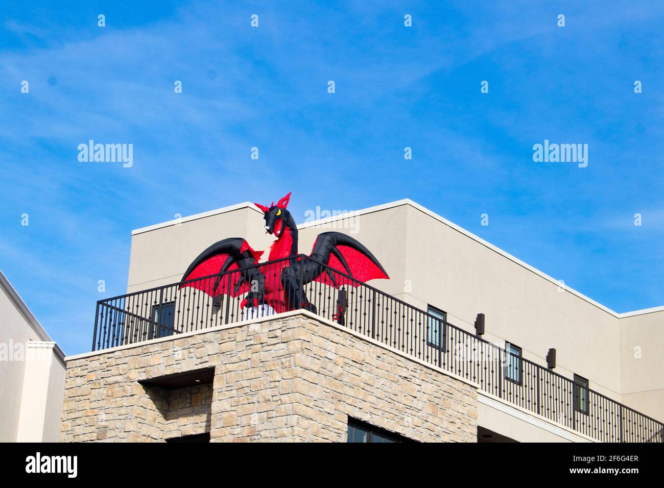 Red and Black blow up dragon on balcony of business building against blue sky for Halloween Stock Photo