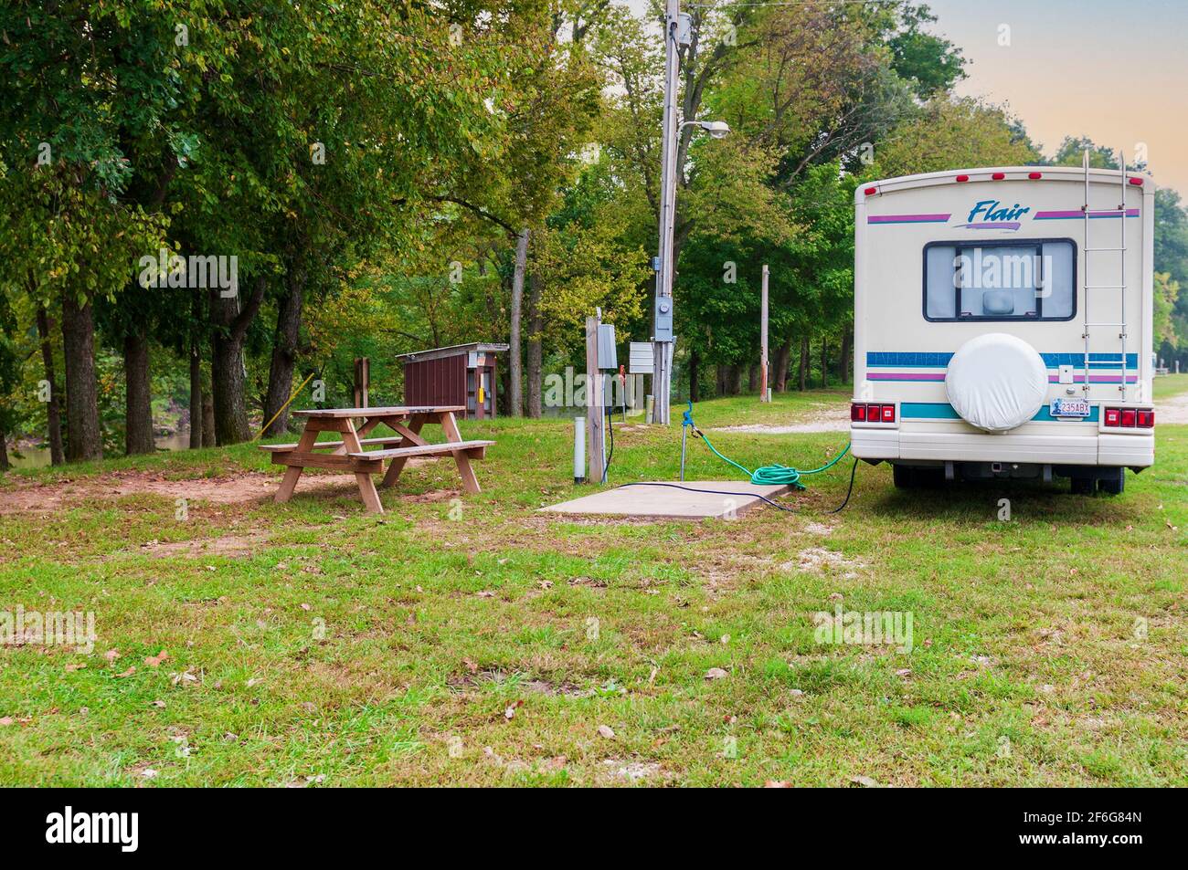 An older class A Flair RV camper van motor home parked at a campsite with water & electrical hookups and a picnic table. USA Stock Photo