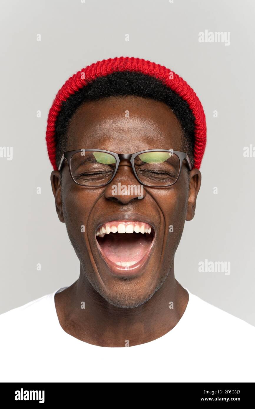 Laughing positive young African hipster man in glasses and red hat in good mood with closed eyes Stock Photo