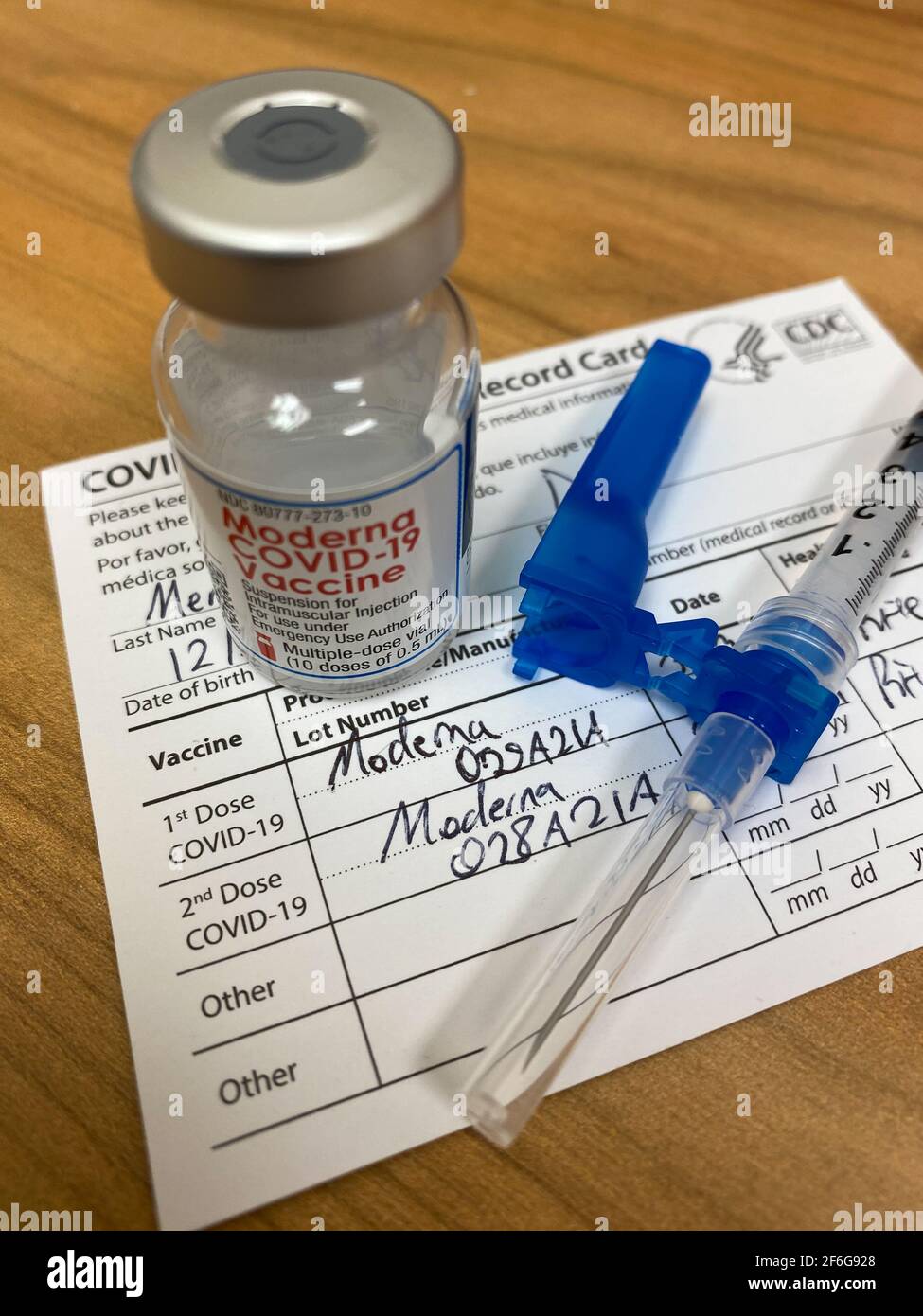 A Moderna COVID-19 vial / 10 dose bottle, needle, and CDC record card with 2nd vaccine dosage indicated. The CDC announced that the Moderna and Pfizer vaccines also prevent asymptomatic infection of the coronavirus. CDC vaccination card can potentially be used as a COVID-19 passport. Stock Photo