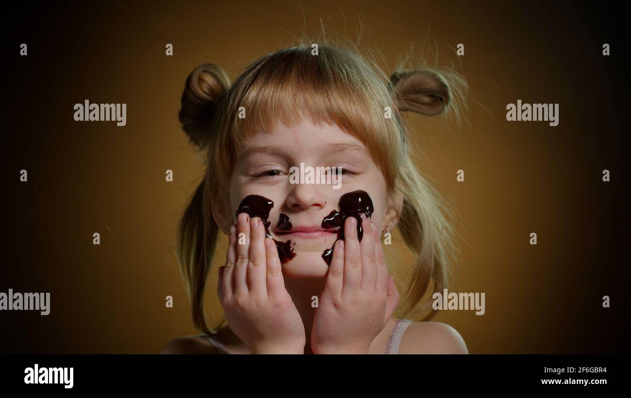 Portrait of teen child kid smears face with melted dark chocolate and starts eating chocolate bar Stock Photo