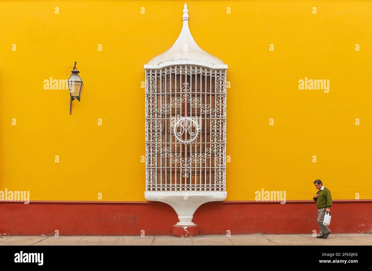 Senior peruvian man walking with blurred motion in front of a colonial style facade with window, Trujillo, Peru. Stock Photo