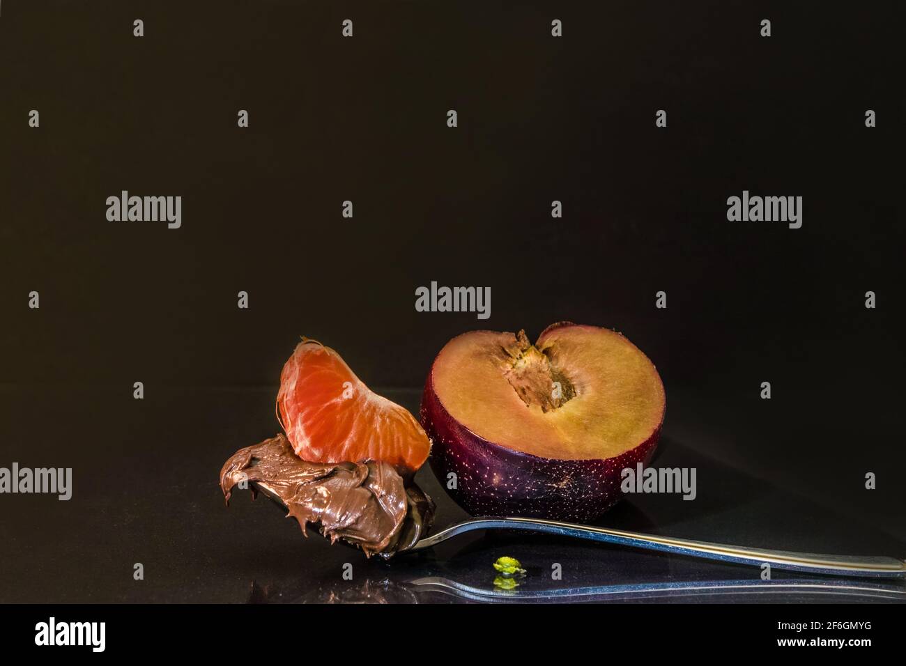 On a spoonful of chocolate we have a slice of blood orange, next to it, half a plum. Low key. Stock Photo