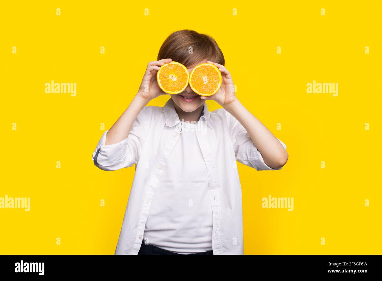 Caucasian boy is covering his eye with sliced lemons smiling on a yellow studio wall Stock Photo