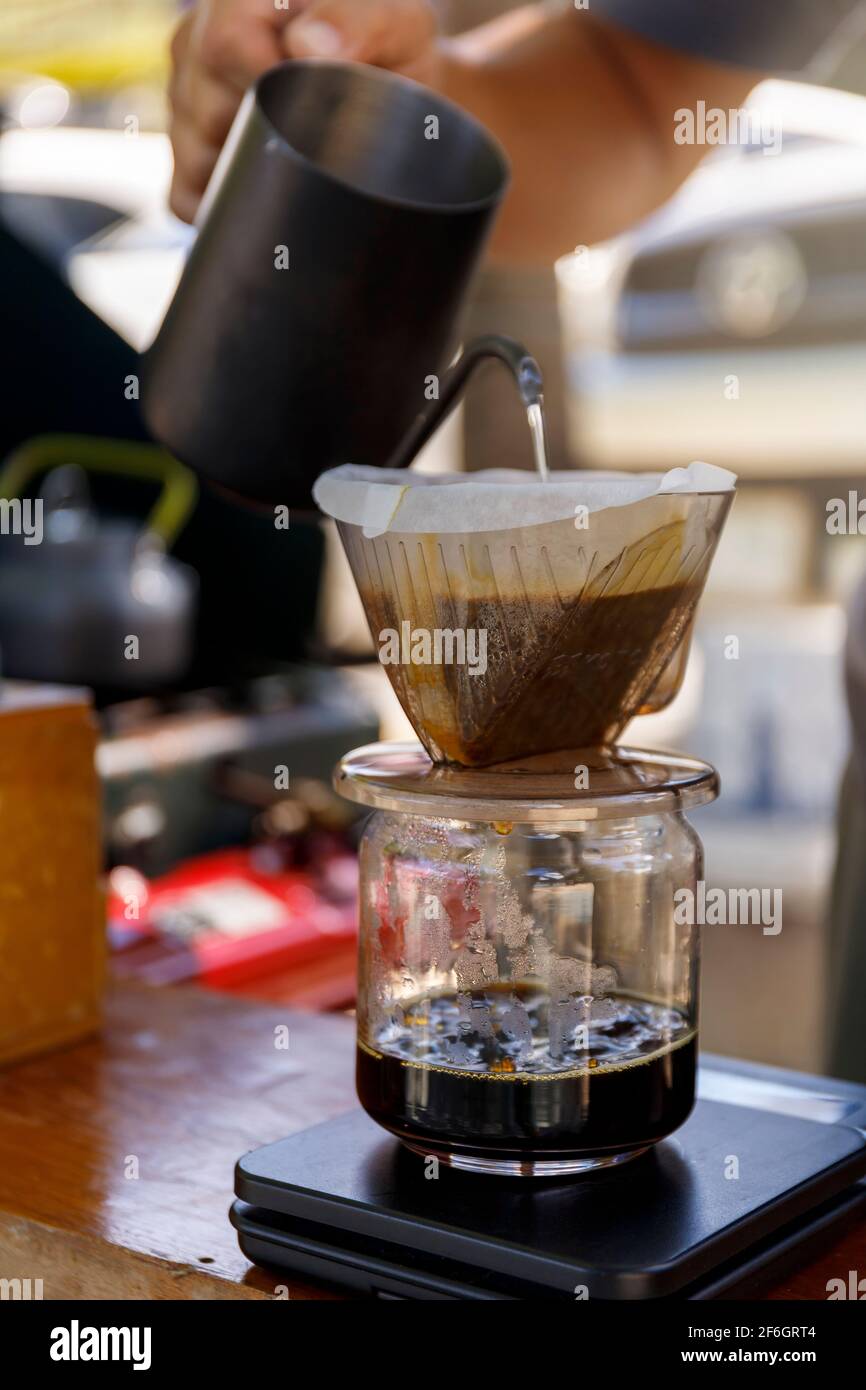 Barista spills hot water prepare filter coffee from stainless steel teapot to drip paper maker on black simple weights. Everything thick wooden table Stock Photo