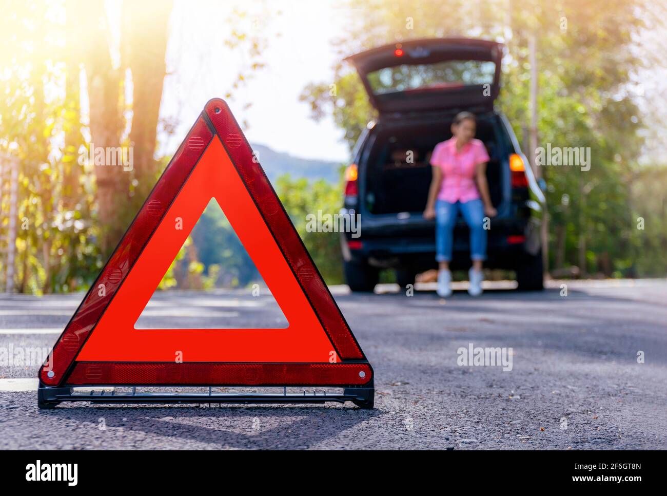Close up red emergency stop sign standing on road. Worried and angry woman walking near his broken car talking on phone with insurance agent. Close up Stock Photo