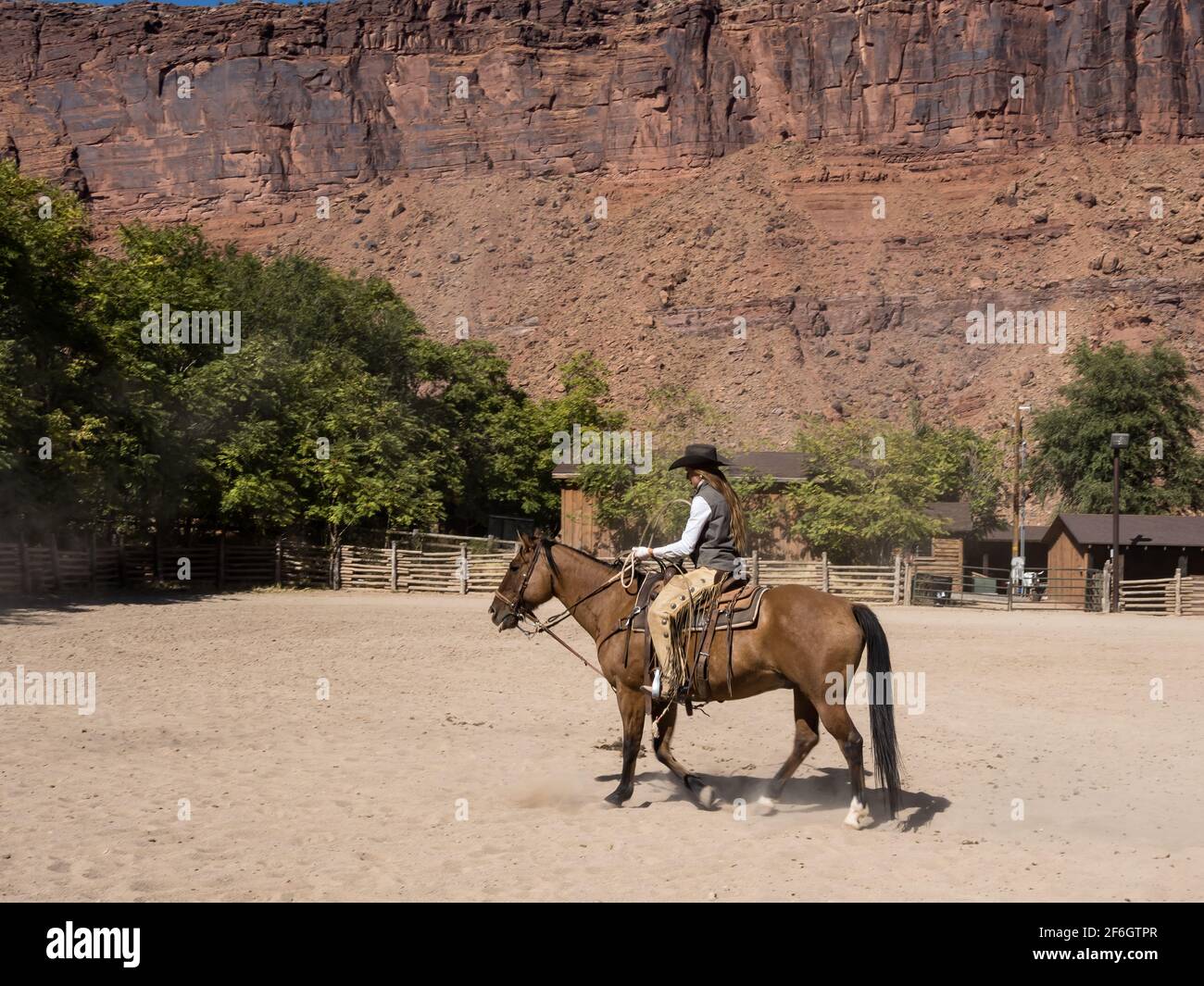 A cowgirl wrangler riding her horse in a corral on a ranch near Moab, Utah.  She wears leather chaps to protect her legs from thorny brush on the rang Stock Photo