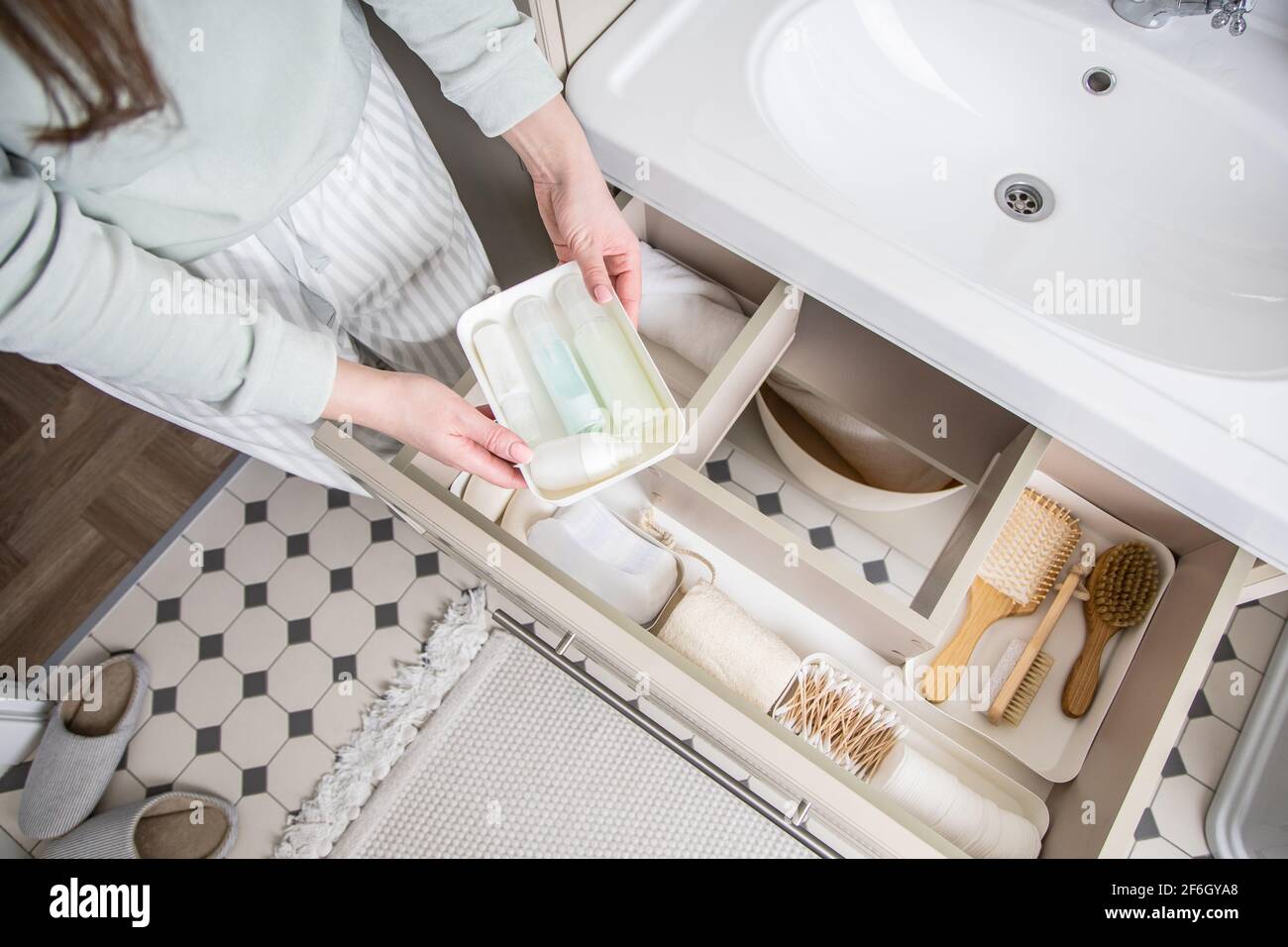 Housewife hands putting rolled up towel into drawer under sink