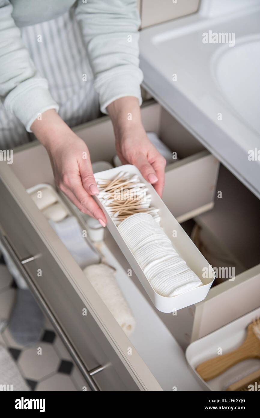 Housewife hands putting rolled up towel into drawer under sink