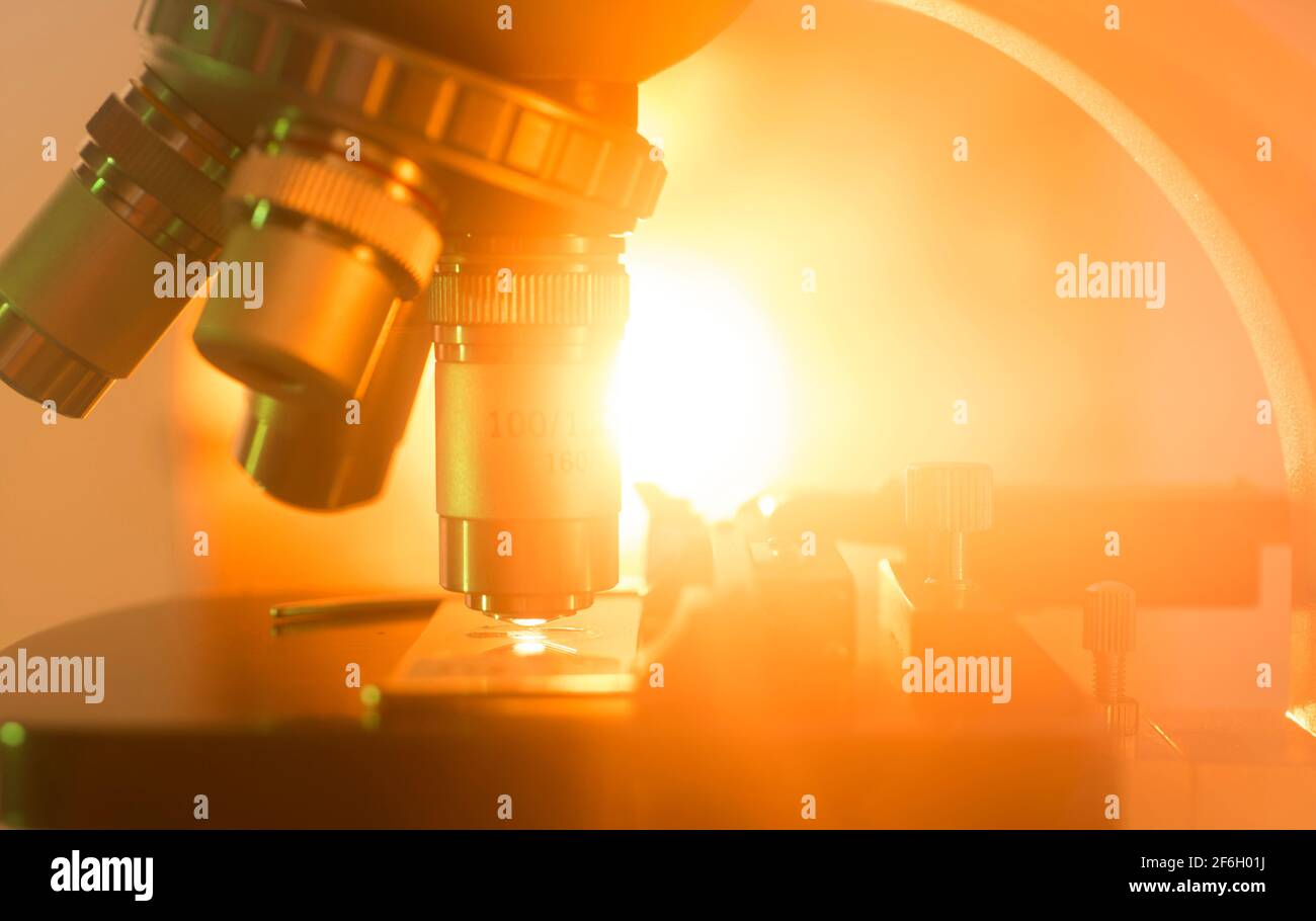 Detail shot of microscope lens with orange light against colored background Stock Photo