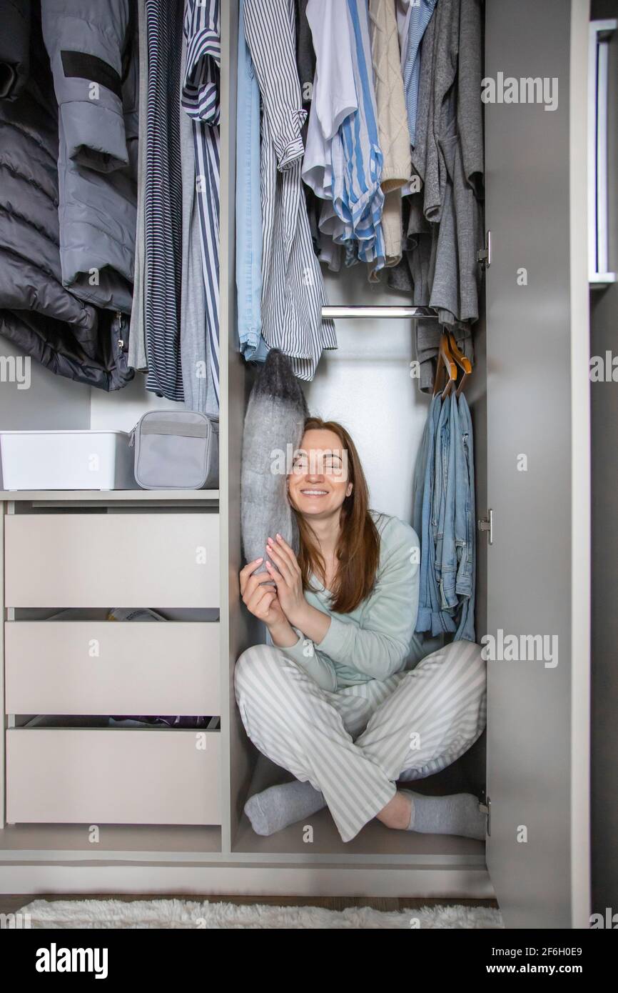 Smiling housewife in pajamas sleeping on pillow at wardrobe. Woman hiding in modern cupboard Stock Photo