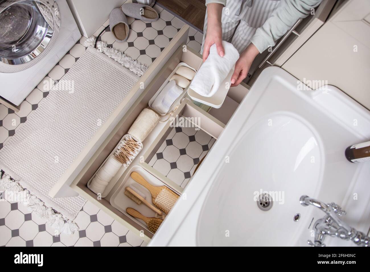 Housewife hands putting rolled up towel into drawer under sink