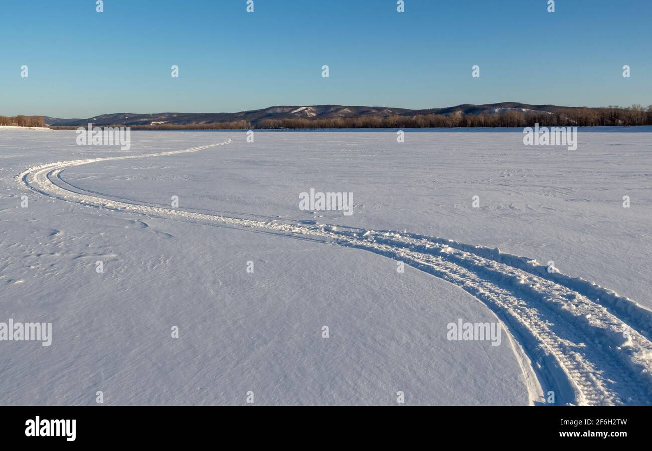 Long winding trails from a motorcycle snowmobile on the surface of a frozen river. Stock Photo