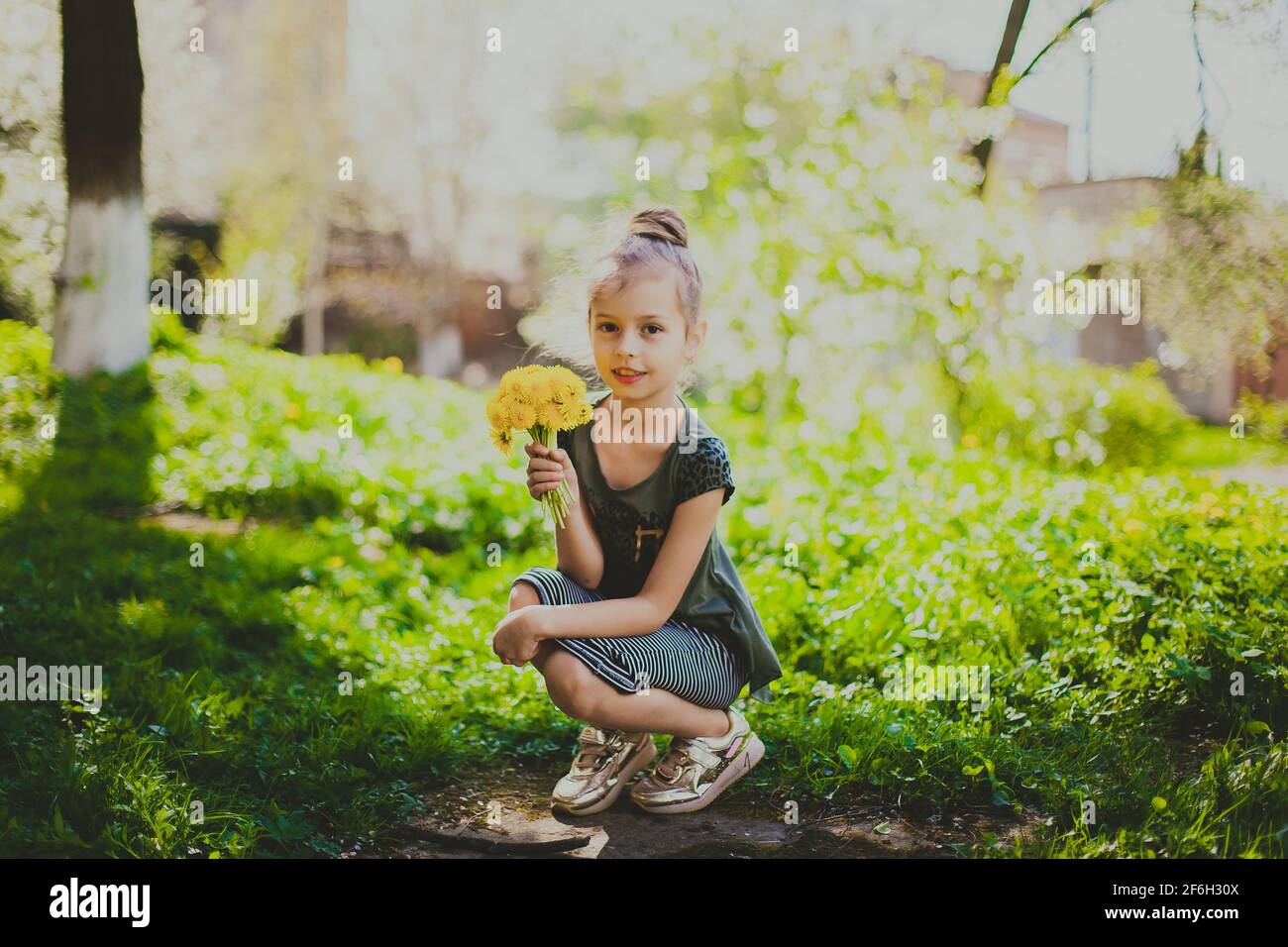 A girl in dress sniffs a bouquet of yellow dandelions in spring cherry garden Stock Photo
