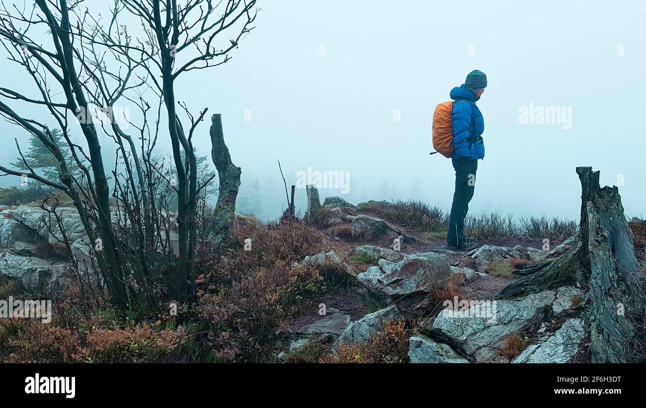 Outdoor hiker woman with backpack and thick clothes in the fog on rock ledge rugged barren nature wasteland mountains mountains Harz Alps Norway Swede Stock Photo