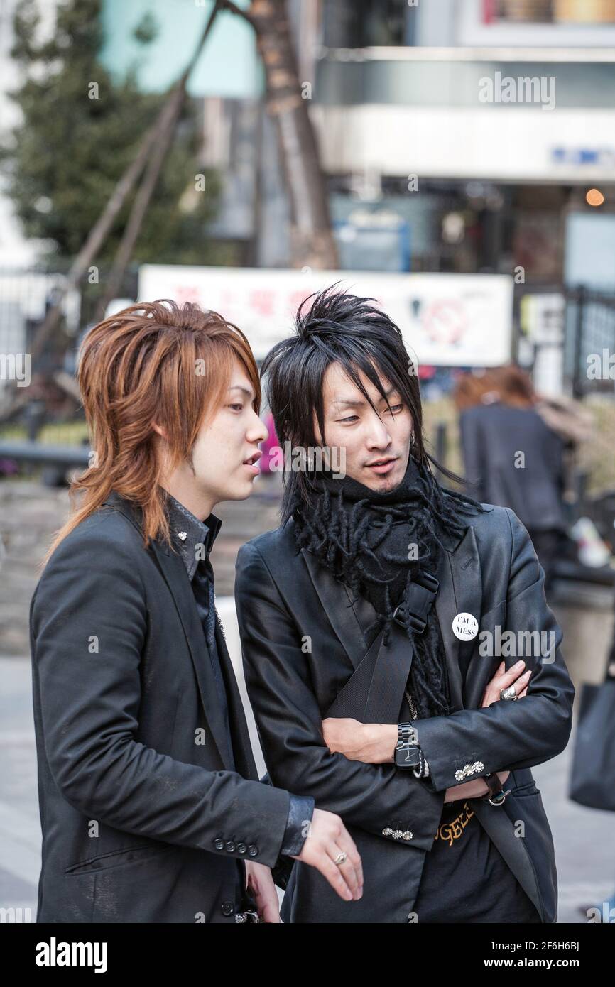 Two Japanese male hosts dressed like rockstars discussing potential victims outside Shinjuku JR train station, Tokyo, Japan Stock Photo