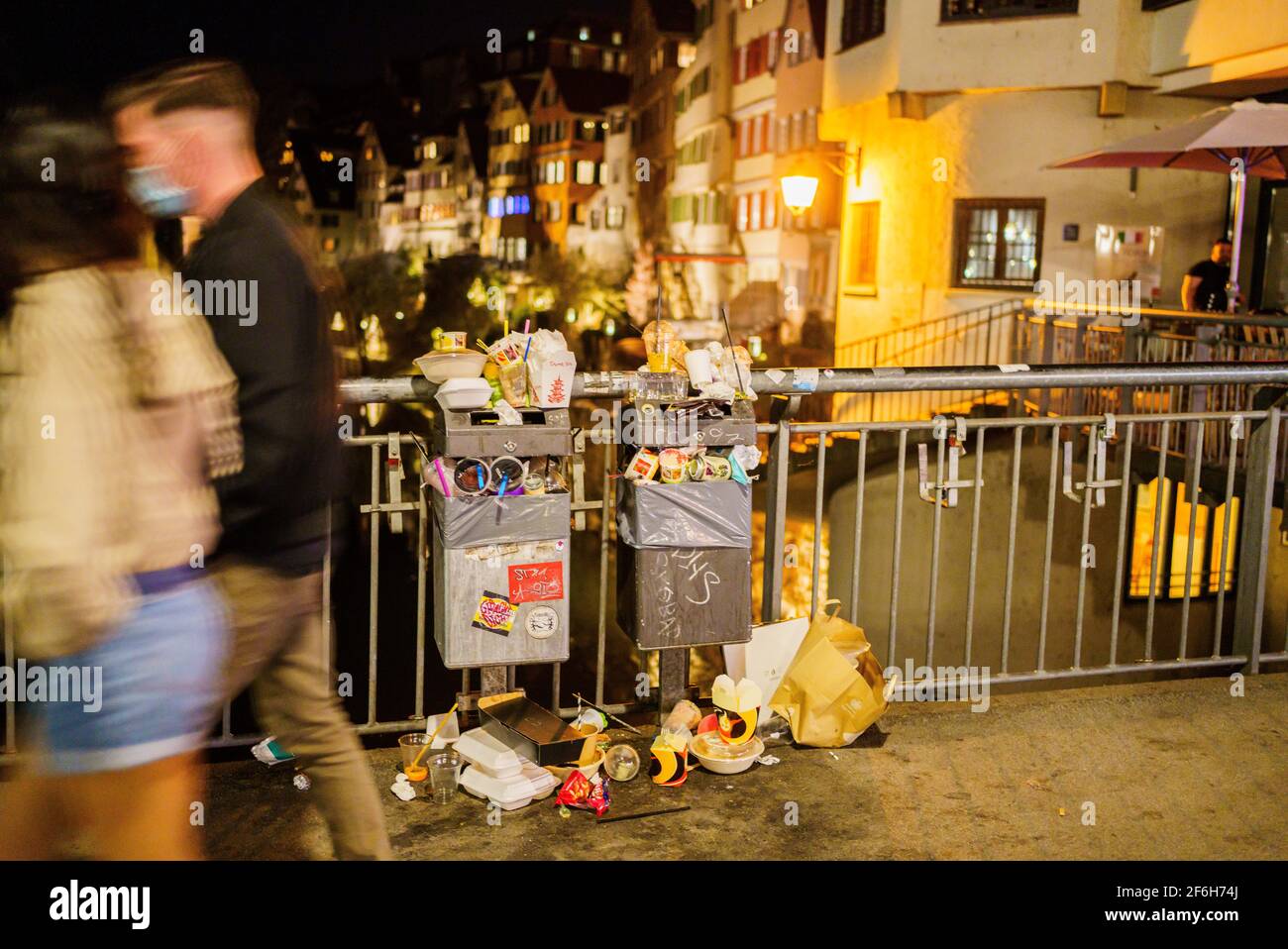 31 March 2021, Baden-Wuerttemberg, Tübingen: Two revellers walk past overflowing rubbish bins on the Eberhardsbrücke. Until now, a day ticket in Tübingen allowed access to restaurants and retail outlets even for out-of-town guests. The city is now significantly restricting the project due to increasing numbers of cases. The day ticket was only issued in case of a negative Corona quick test. Photo: Andreas Arnold/dpa Stock Photo