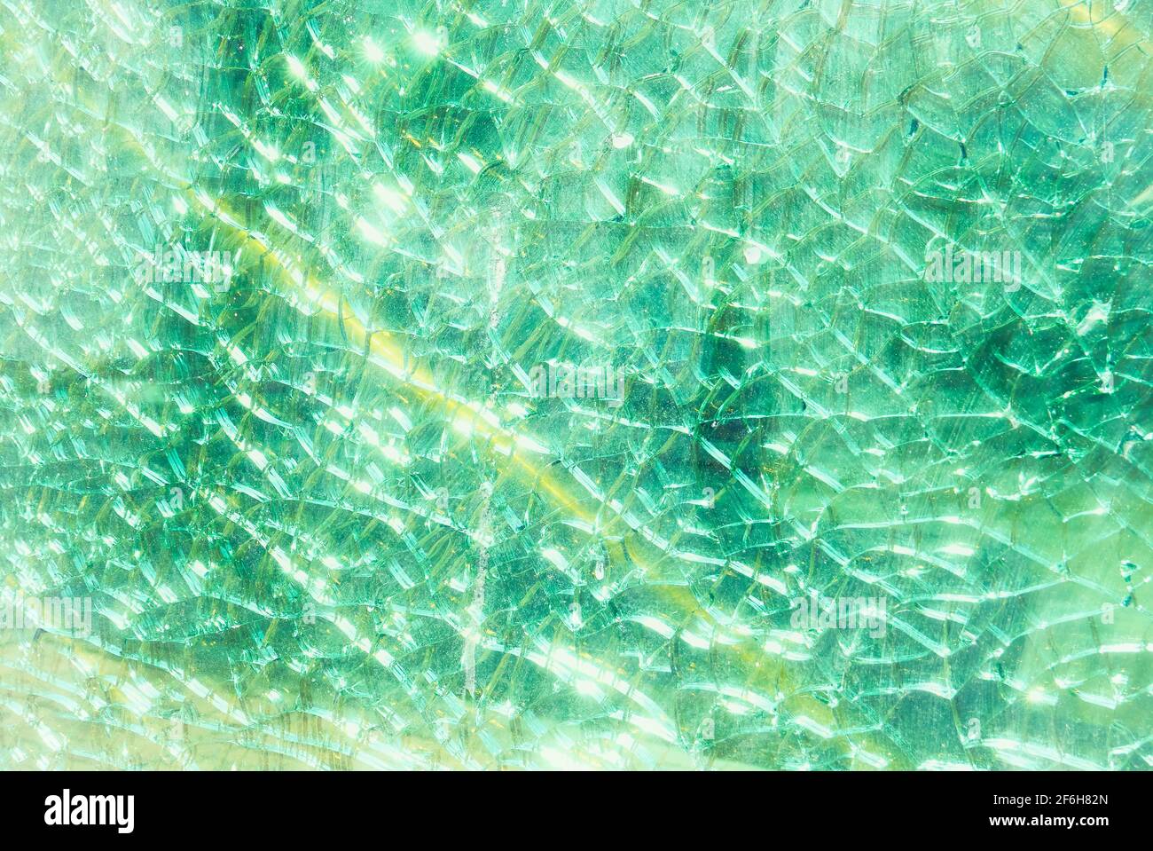 Close-up of a pastel green colored broken fragmented glass window shield, with a yellow line Stock Photo