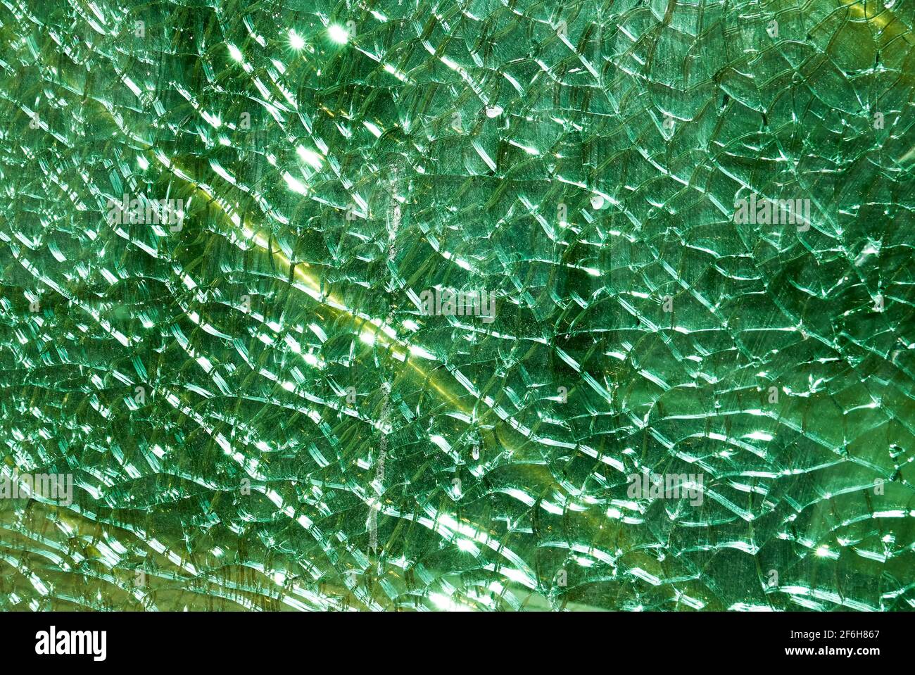 Close-up of a green colored broken fragmented glass window shield, with a yellow line Stock Photo
