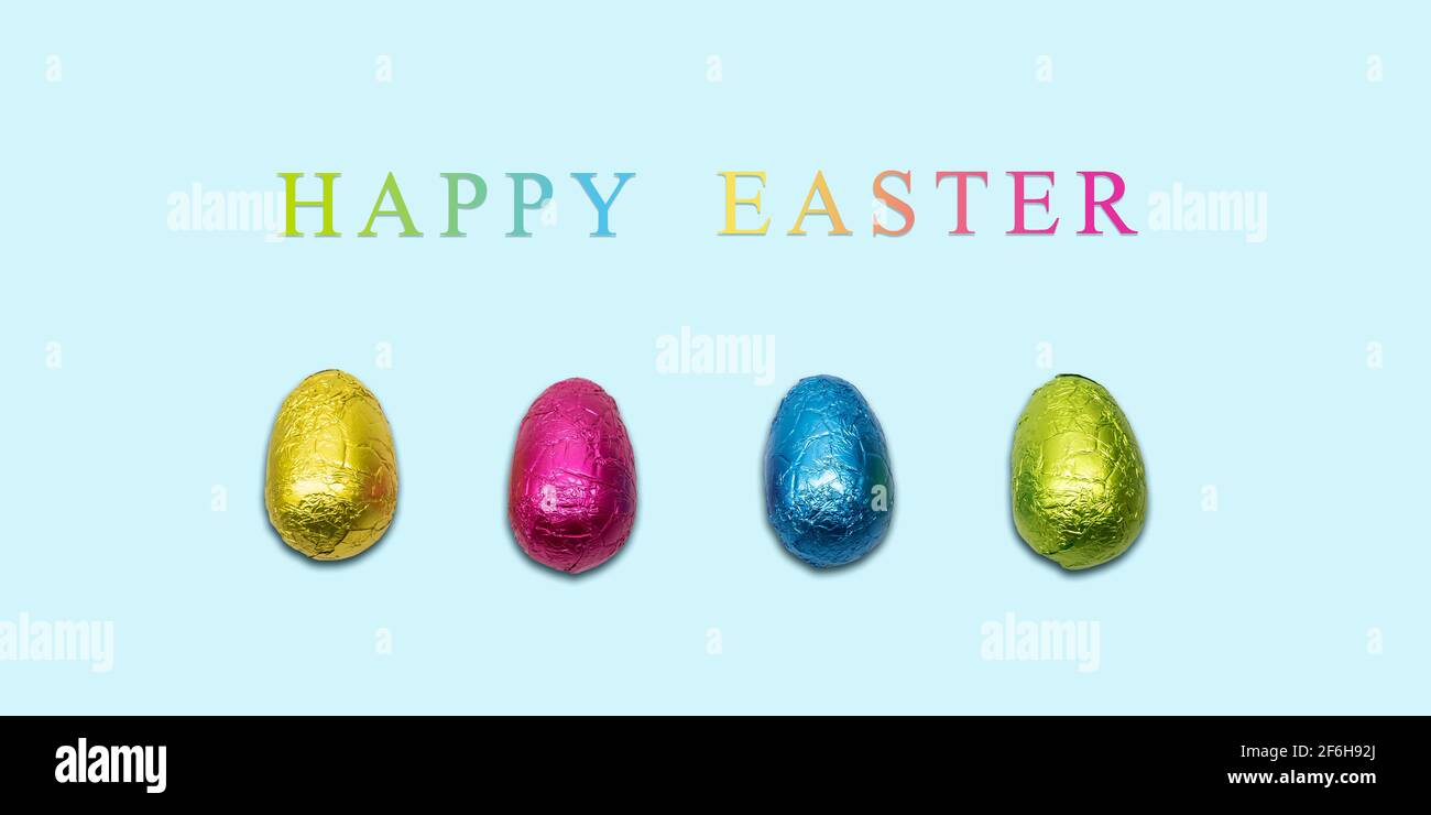 Happy Easter card with wrapped chocolate eggs on blue background. Minimal design. Stock Photo