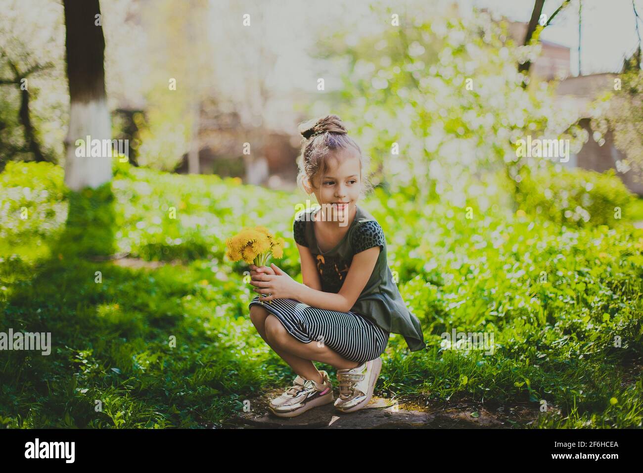 A girl in dress holds a bouquet of yellow dandelions in spring cherry garden Stock Photo