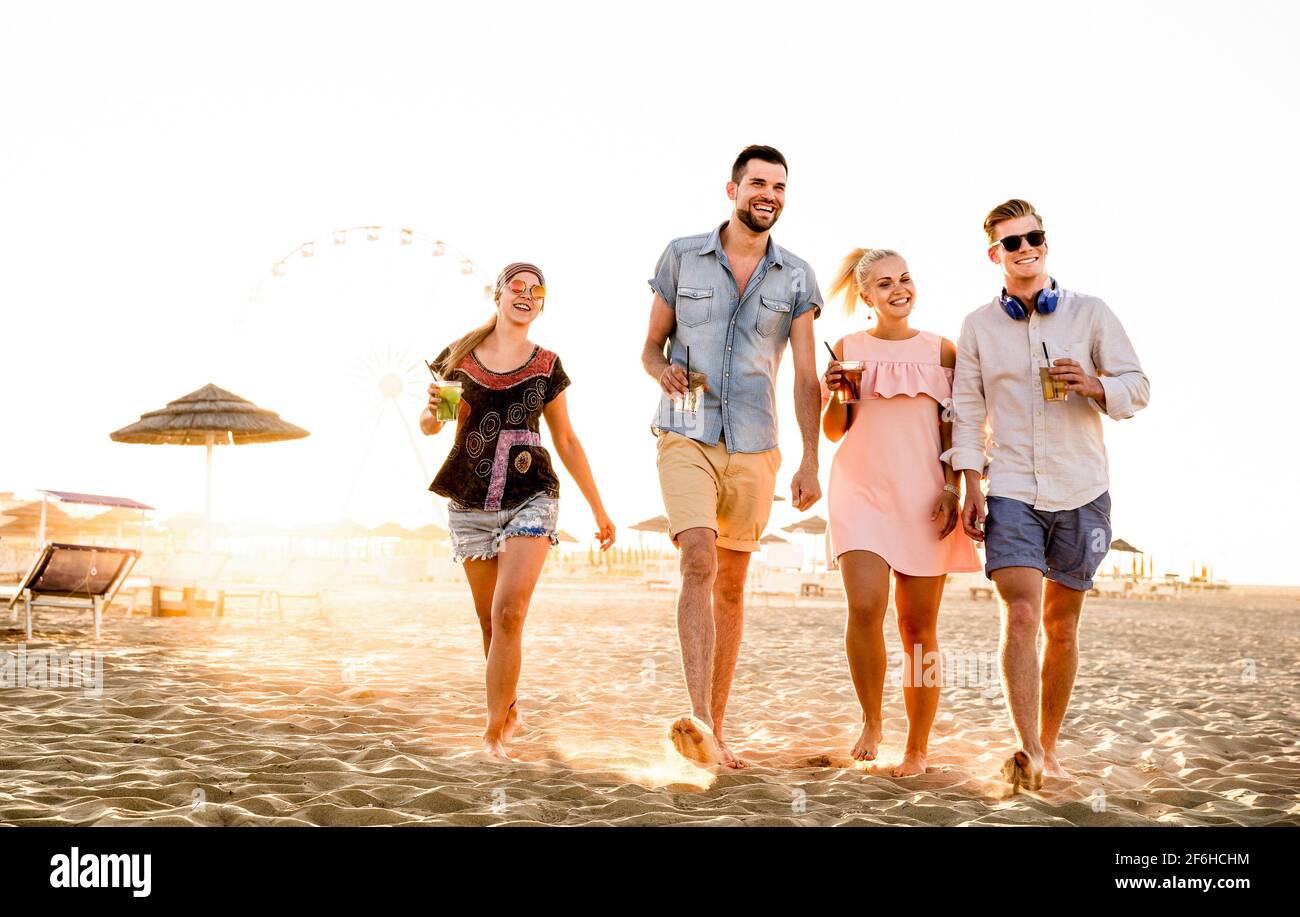 Group of happy friends having fun at seaside sunset - Summer vacations and friendship concept with young people millennials walking at beach Stock Photo