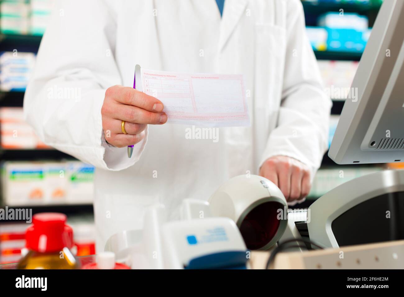Pharmacist in pharmacy, standing at the cashier he is holding a prescription slip in his hands Stock Photo