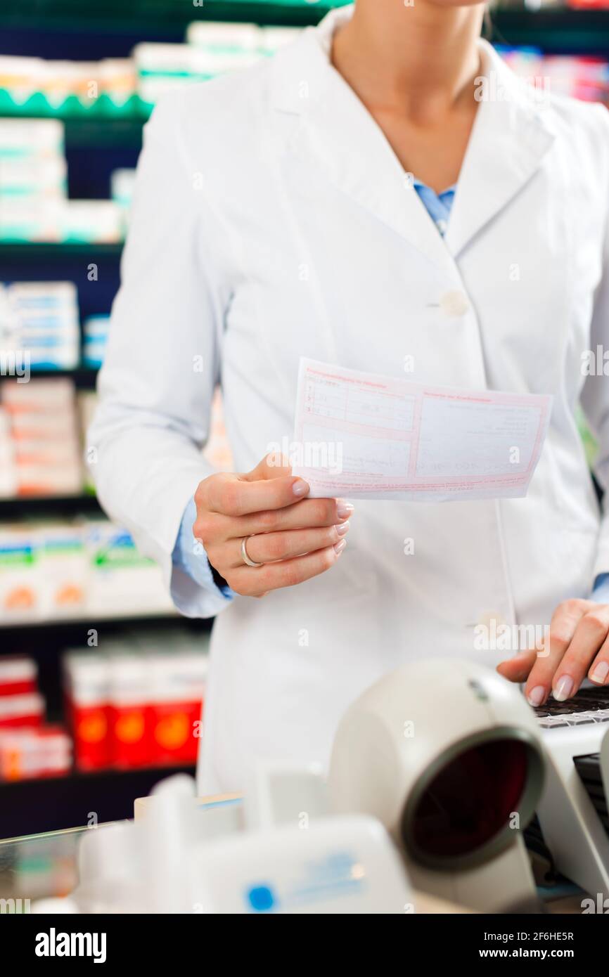 Female Pharmacist in pharmacy, standing at the cashier she is holding a prescription slip in her hands Stock Photo
