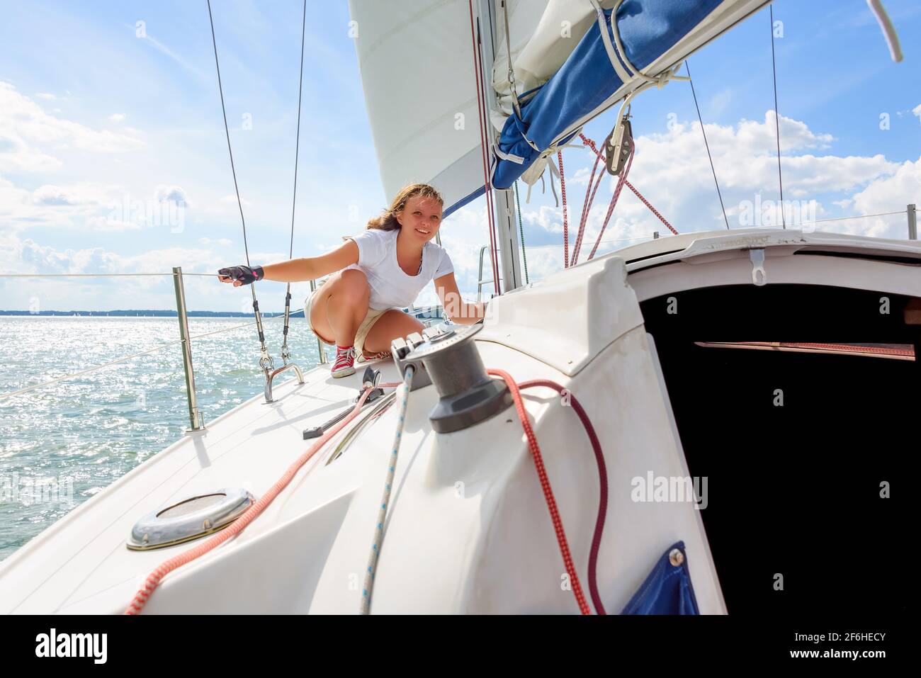 Young woman sailing on a yacht. Female sailboat crewmember trimming main sail during sail on vacation in summer season Stock Photo