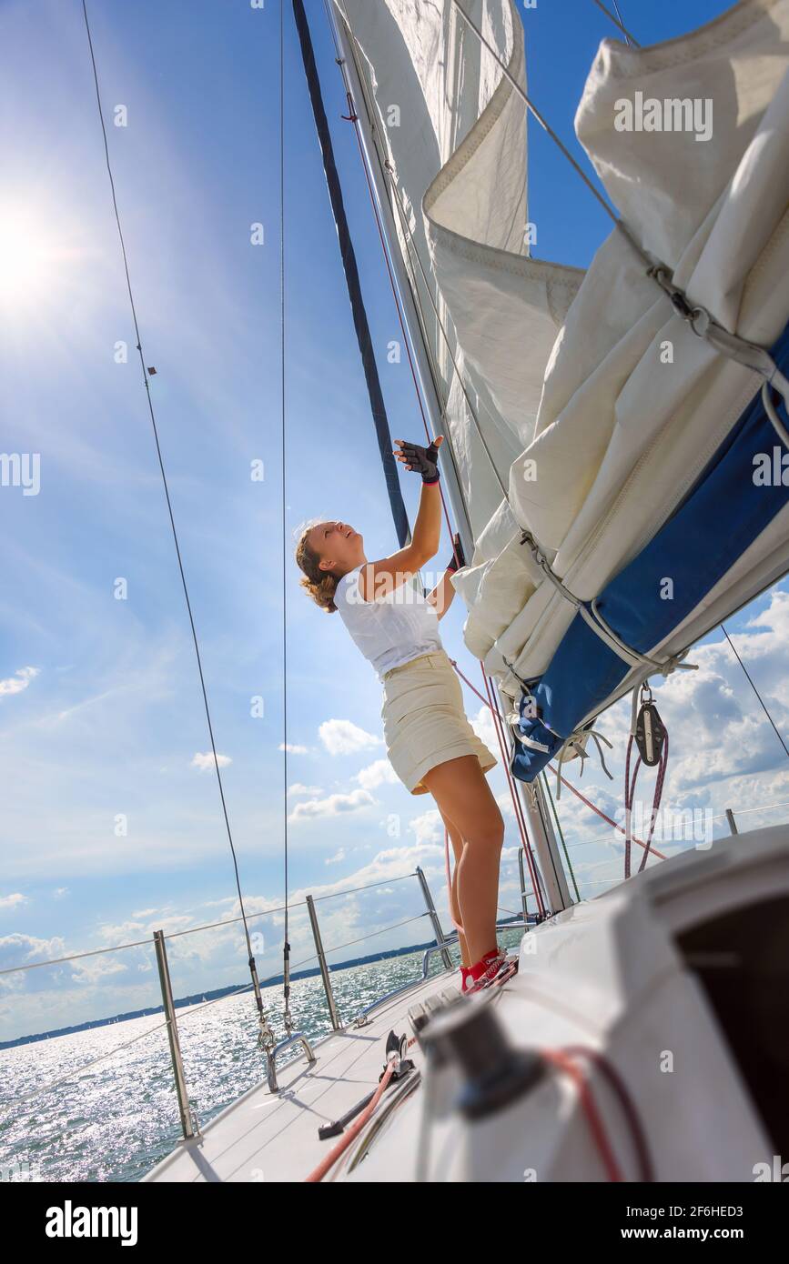 Young woman sailing on a yacht. Female sailboat crewmember trimming main sail during sail on vacation in summer season Stock Photo