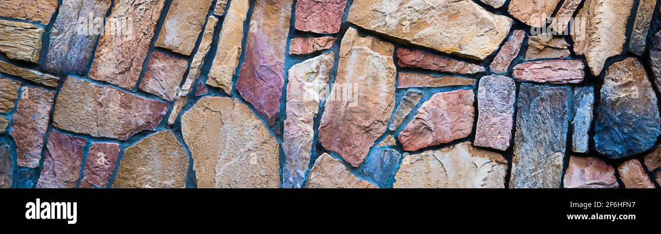 The wall is made of multi-colored natural stone, the masonry is stone