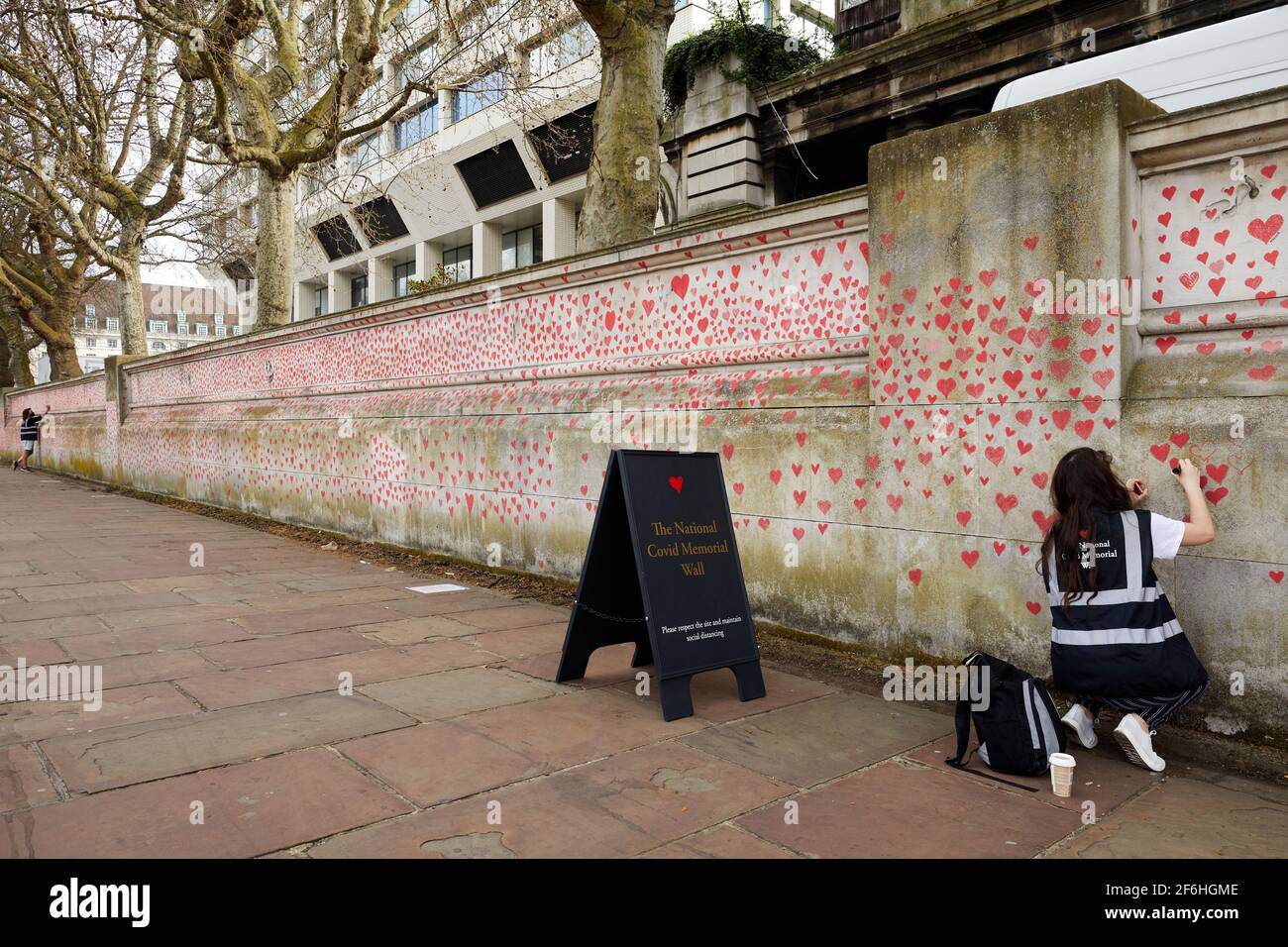 London, UK - 31 Mar 2021: Family and friends of Covid-19 victims paint red hearts at the National Covid Memorial Wall in front of St. Thomas' Hospital in central London. Each individually drawn heart  represents a victim of the coronavirus virus. Stock Photo