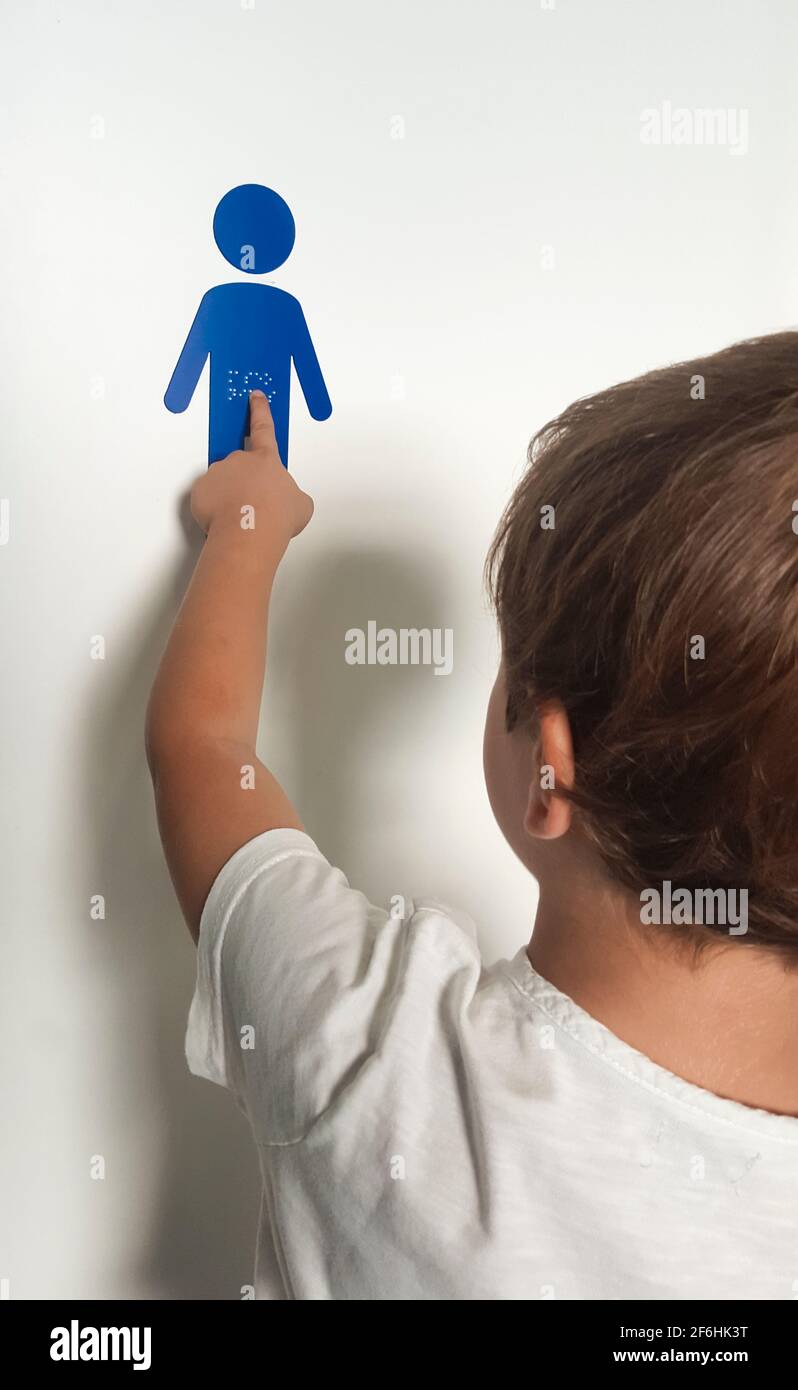 Child boy touching braille sticker sign at children toilet door. Blind children accessibility concept Stock Photo