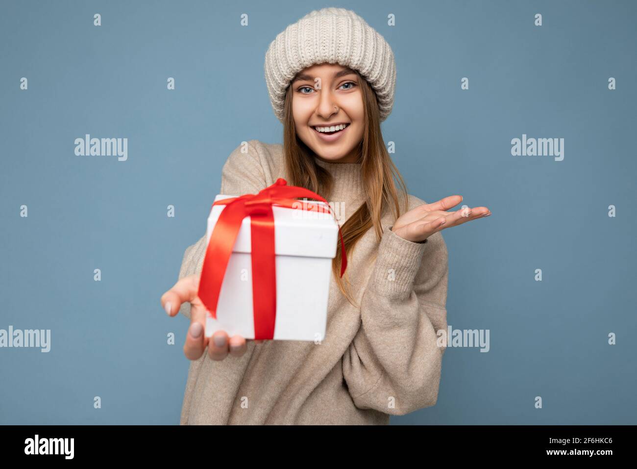 Beautiful happy young dark blonde woman isolated over colourful background wall wearing stylish casual clothes holding gift box and looking at camera Stock Photo