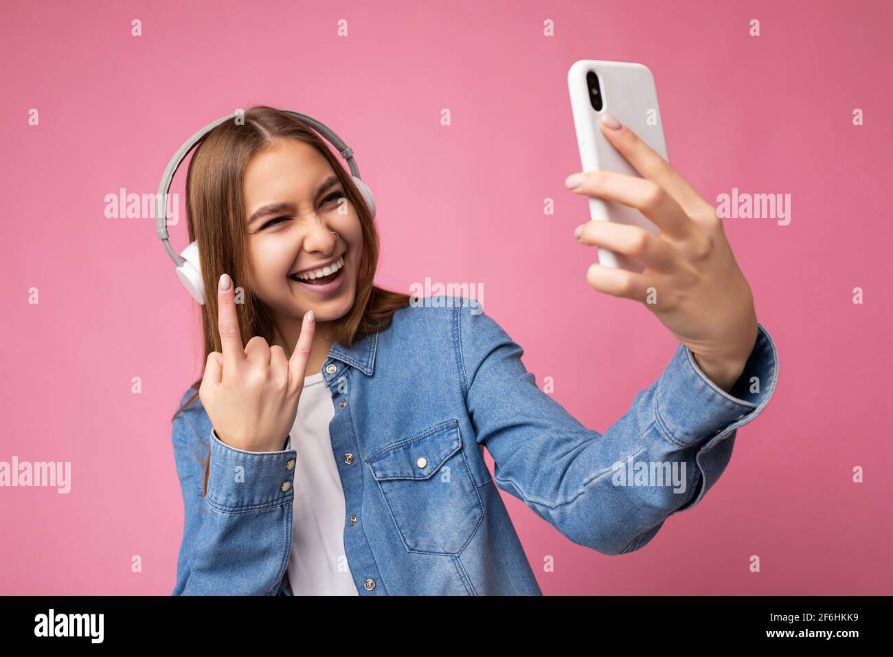 Close-up Photo of beautiful positive laughing young dark blonde woman wearing blue jean stylish shirt and casual white t-shirt isolated over pink Stock Photo
