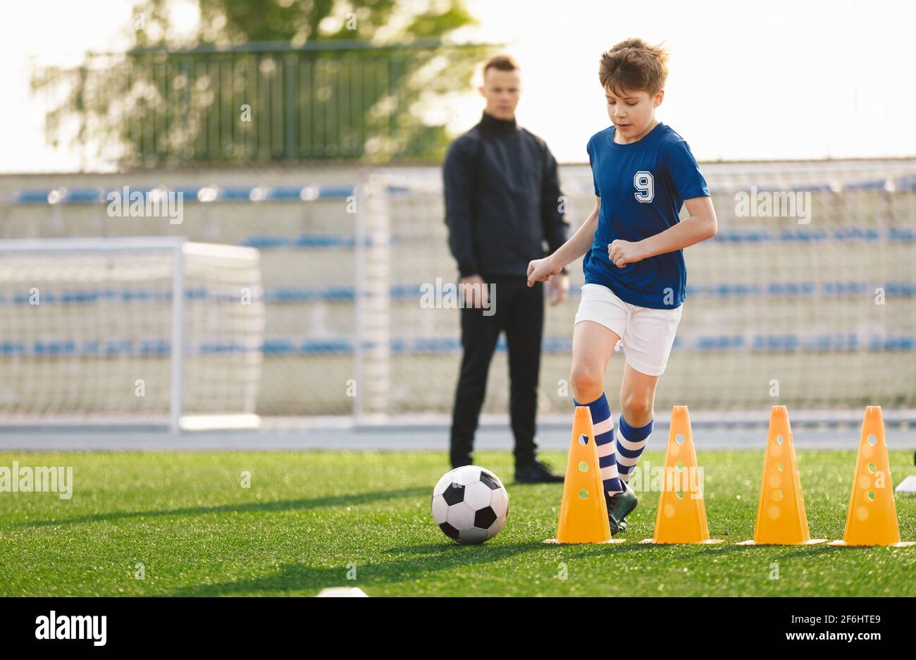 Sporty Soccer Boys Running Ball on Training Drill. Young Coach Watching Youth Football Team Practice Session. Kid Kicking Soccer Ball on Soccer Traini Stock Photo