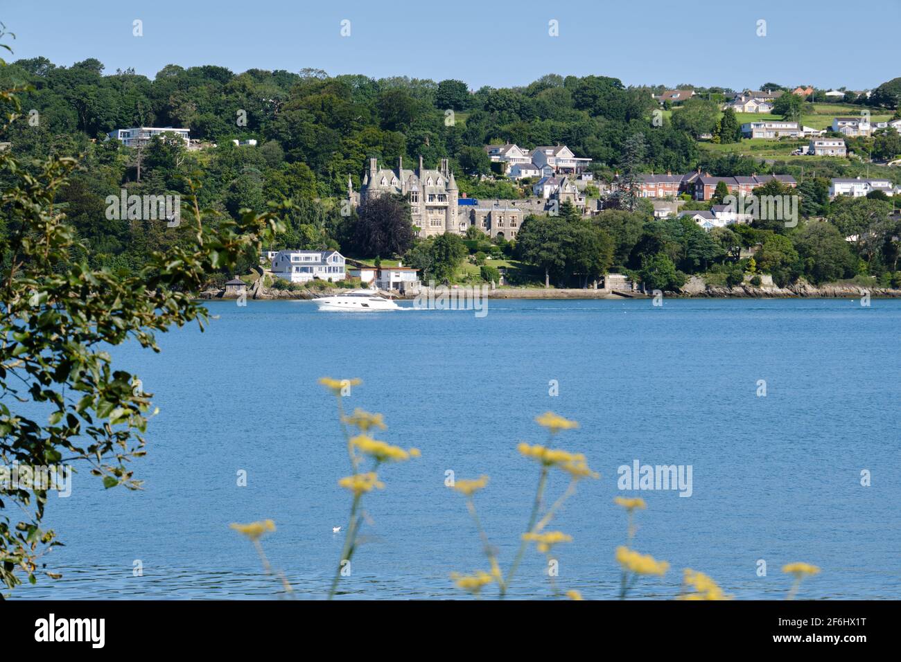 A large luxury motorboat crosses in front of Château Rhianfa along the Menai Strait, Wales Stock Photo