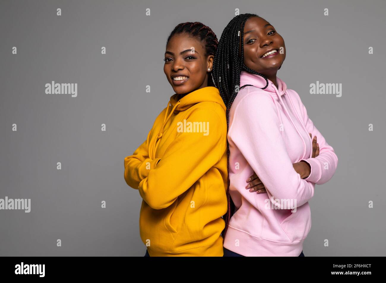 Portrait of two happy african women smiling while standing back to back ...