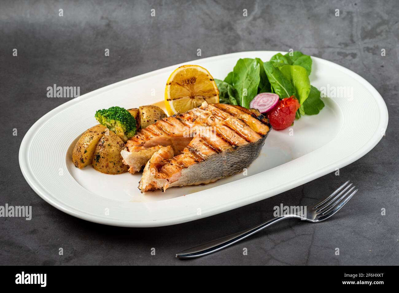 plate of grilled salmon steak with vegetables on dark stone table Stock ...